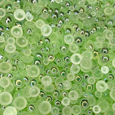 A close-up view of a mix of transparent iridescent green acrylic pearls of various sizes.
