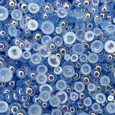 A close-up view of flat-back transparent iridescent acrylic pearls in various sizes, intended for use as embellishments.