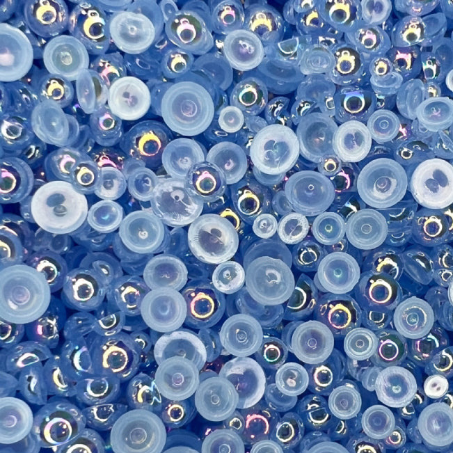A close-up view of flat-back transparent iridescent acrylic pearls in various sizes, intended for use as embellishments.