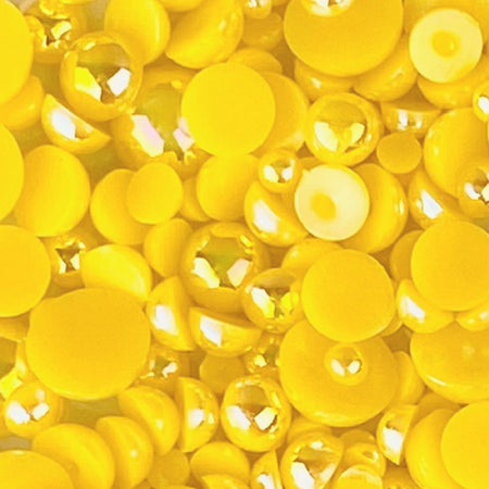 A close-up of yellow acrylic flat-back baubles embellishments in a mix of sizes, with the brand's website address visible.